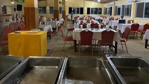 Un salón de banquetes con varias mesas y sillas, una zona de bufé con bandejas de metal y un techo de madera.