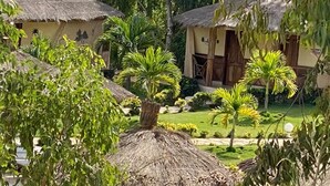 Un edificio tradicional con techo de paja y un jardín bien cuidado, que incluye palmeras y césped.