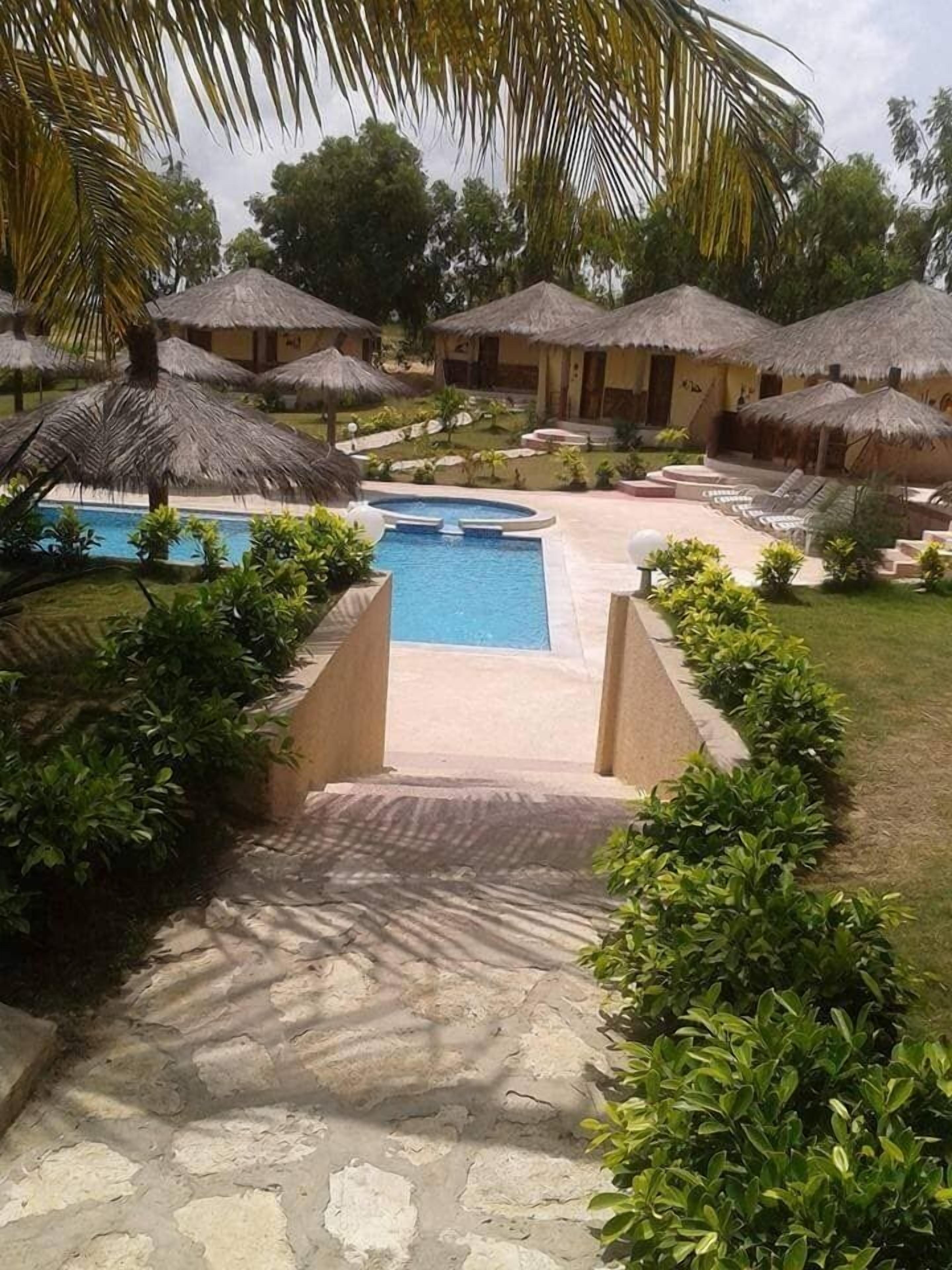 A resort with a swimming pool, thatched-roof huts, and a well-maintained garden.