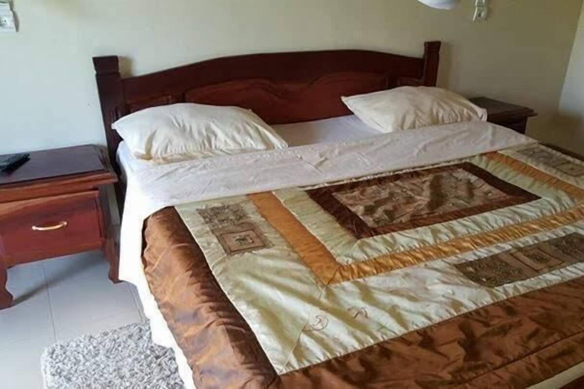 A neatly made bed with a quilt, a wooden headboard, and a nightstand with a drawer.