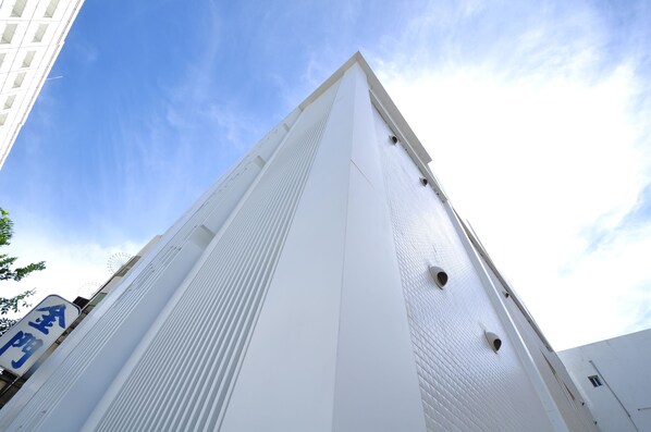 A tall, white building with a modern architectural design, featuring a prominent vertical line pattern and several small windows. - Leesing Hotel (Kaohsiung)