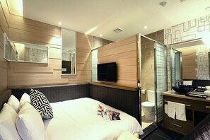 A modern hotel room with a bed, a TV, a bathroom with a glass shower, and a wooden wall design. - Leesing Hotel (Kaohsiung)