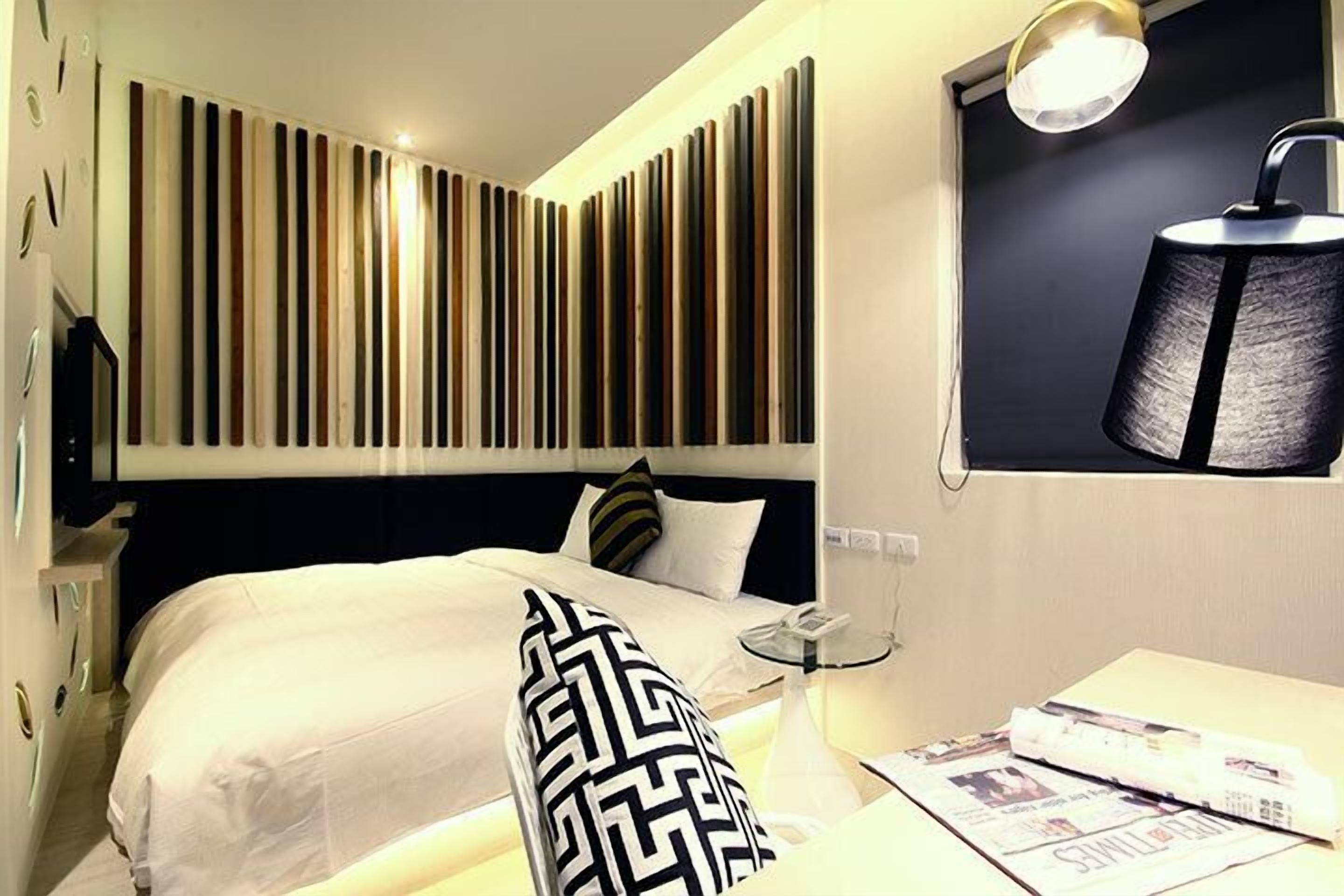 A hotel room with a bed, a bedside table, a lamp, and a wall with vertical wooden slats.