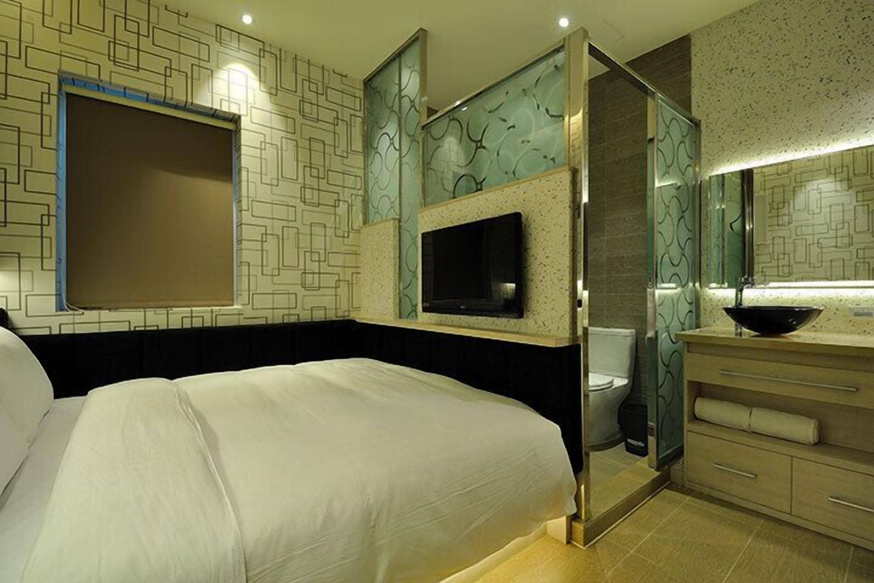 A hotel room with a bed, a television mounted on the wall, a bathroom with a sink and mirror, and a patterned wall design.