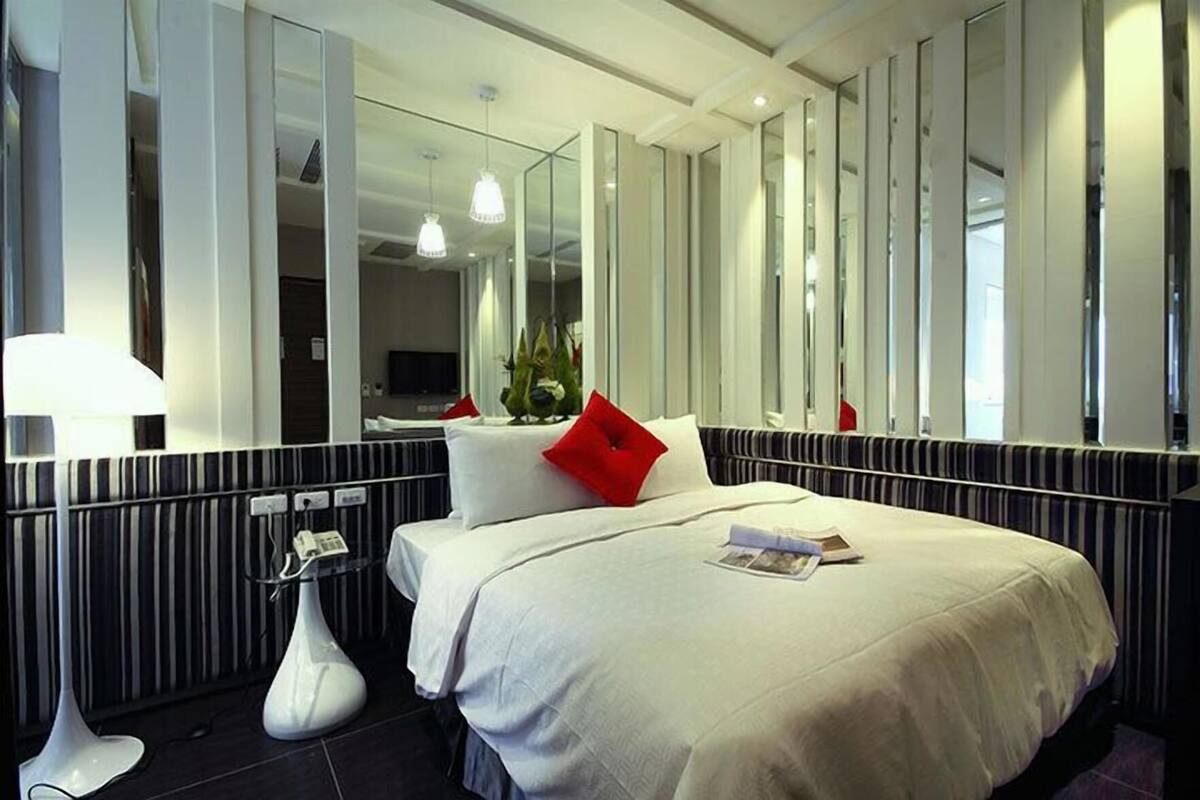 A hotel room with a large bed, a bedside table, a mirror, and a potted plant.