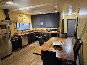 A compact kitchen with a refrigerator, microwave, and sink. There is a dining table with chairs and a window with curtains.