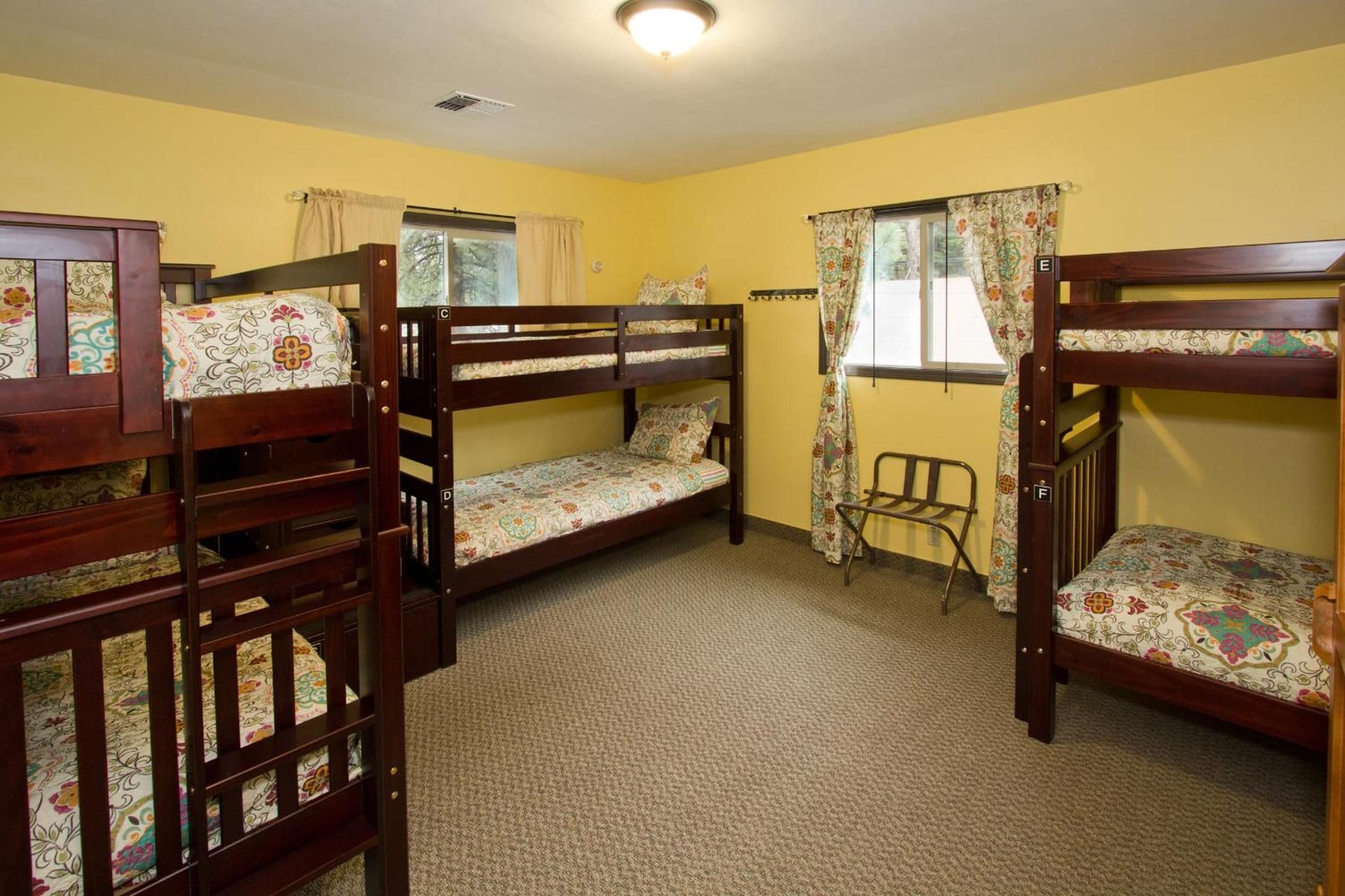 A dormitory room with bunk beds, a small window with curtains, and a radiator.