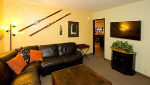 A living room with a black leather sofa, a wooden coffee table, a TV on the wall, and a plant on a cabinet. - Moderne Hostel (Mammoth Lakes)