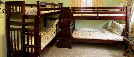 Quarto com beliches de madeira, uma janela com cortinas e piso coberto por carpete.