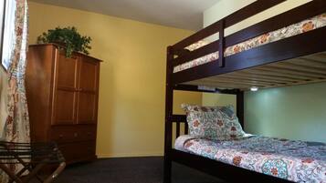 A bunk bed with floral bedding, a wooden wardrobe, and a plant on top.