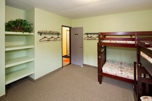 A bunk bed room with a door leading to another room, a shelf with plants, and a coat rack.