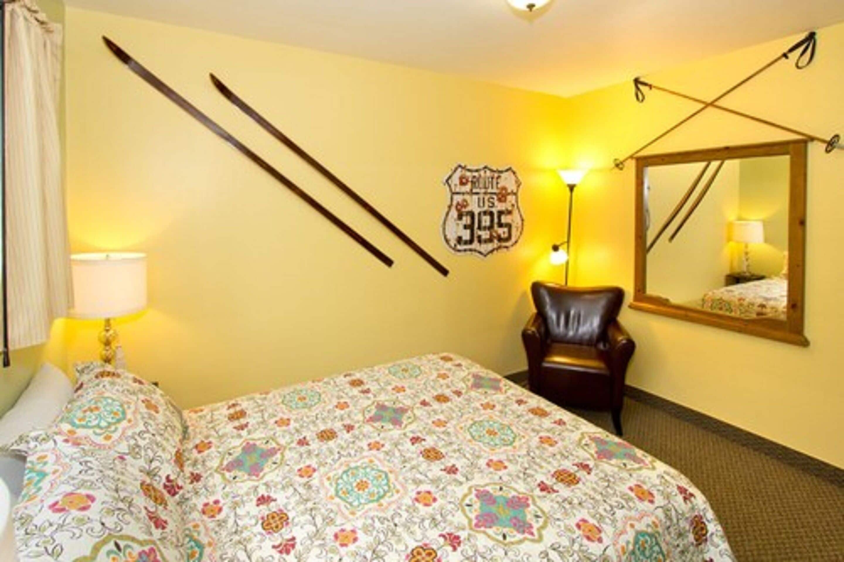 A hotel room with a bed, a chair, a lamp, a mirror, and a wall decoration.