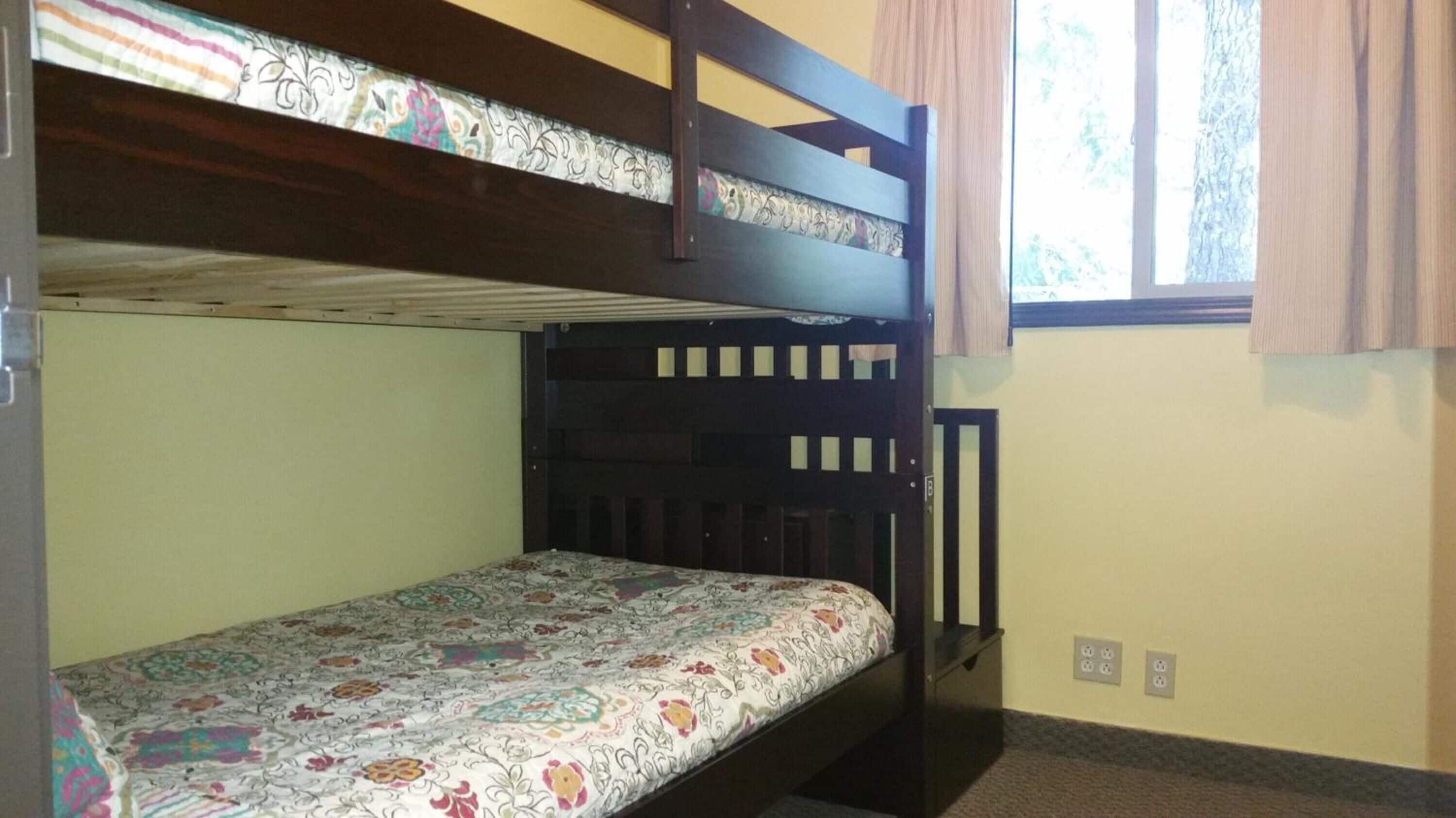A bunk bed room with a patterned bedspread, a window with curtains, and a door with a handle.