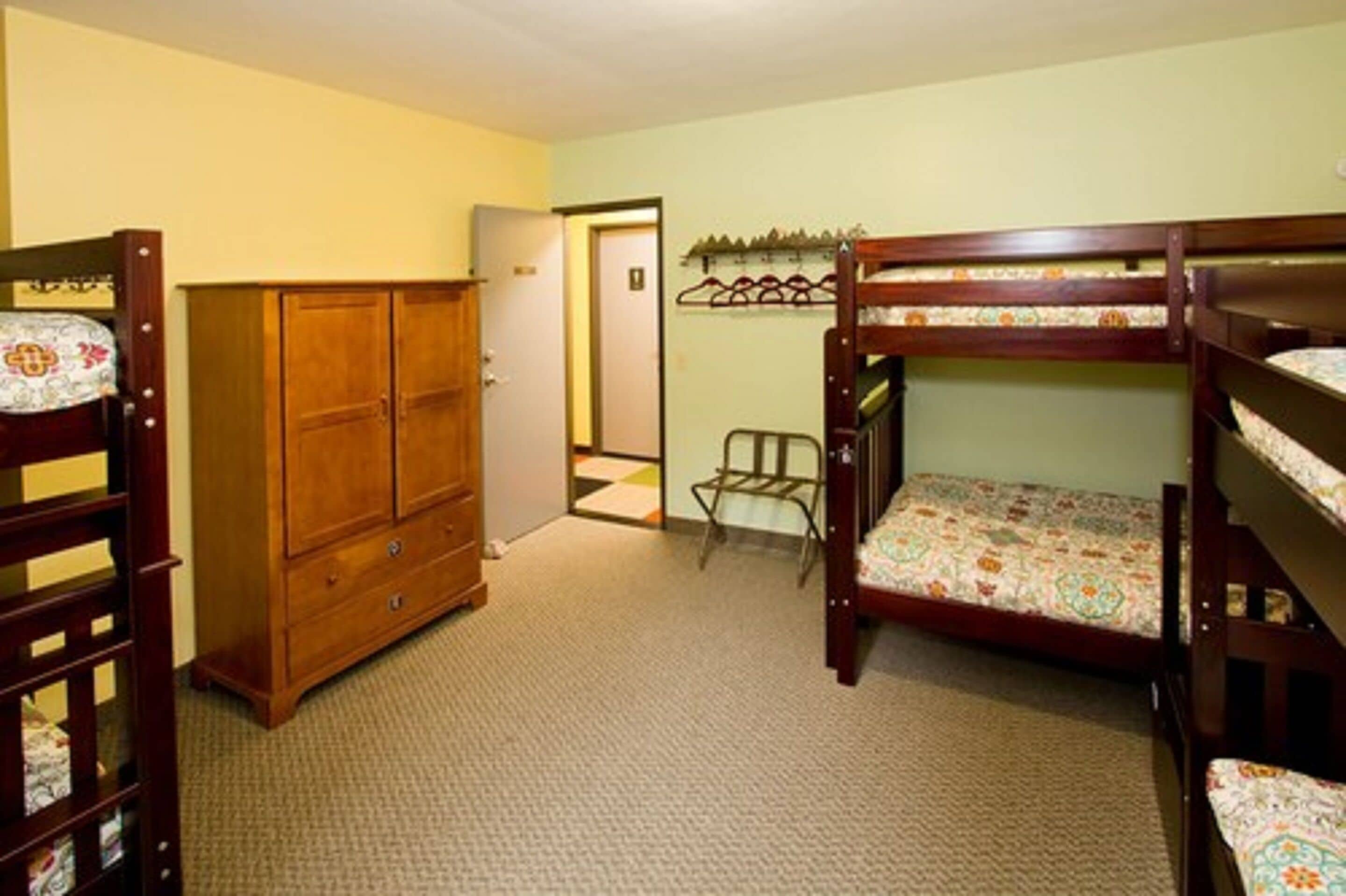Una habitación con literas, un armario de madera y un escritorio pequeño.