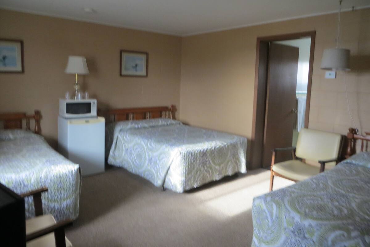A hotel room with two single beds, a desk with a lamp, a chair, a microwave, and a door leading to another room.