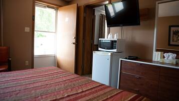 A hotel room with a bed, a dresser, a microwave, a television, and a window.