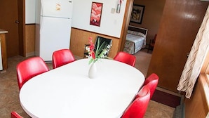 A compact kitchen with a white refrigerator, a dining table with red chairs, and a small flower vase. - Adams Golden Acres Motel (Kingsville)