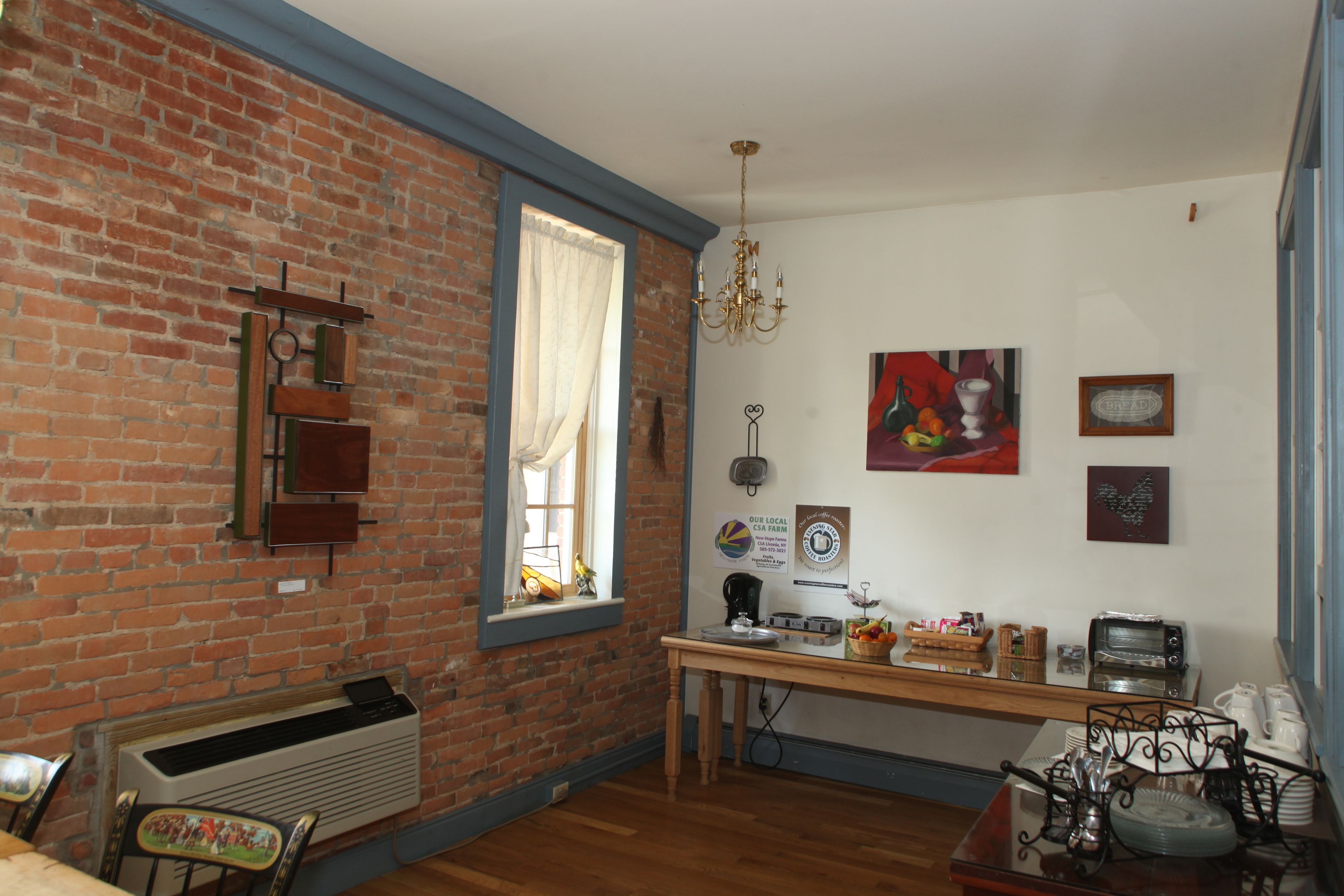 Quarto com parede de tijolos, mesa de madeira, janela com cortinas, um candelabro e várias decorações nas paredes.