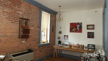 Quarto com parede de tijolos, mesa de madeira, janela com cortinas, um candelabro e várias decorações nas paredes.