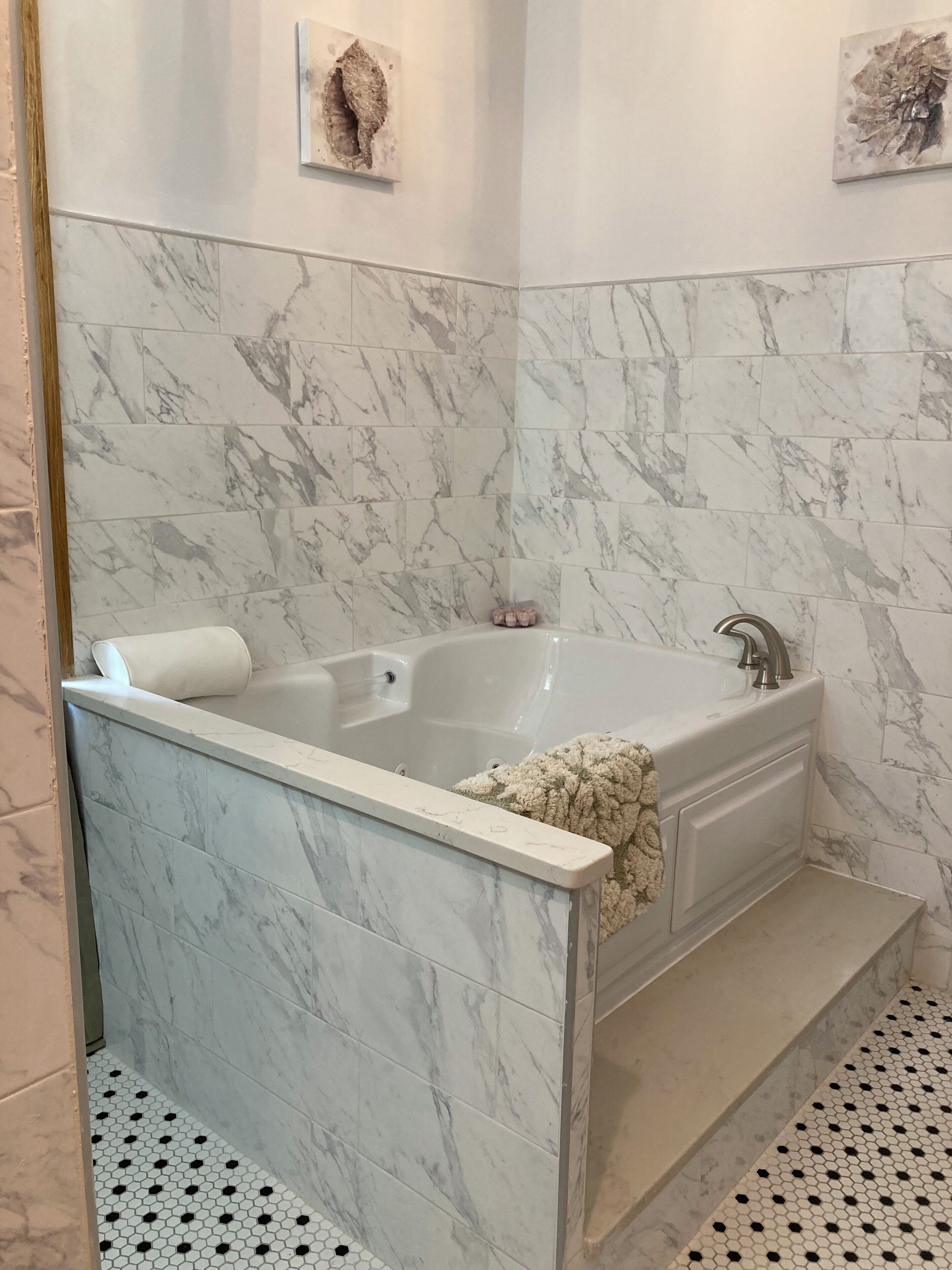 Une salle de bain avec un mur recouvert de carreaux de marbre, une baignoire avec une serviette blanche, et un sol carrelé avec des motifs hexagonaux.