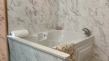 Une salle de bain avec un mur recouvert de carreaux de marbre, une baignoire avec une serviette blanche, et un sol carrelé avec des motifs hexagonaux.