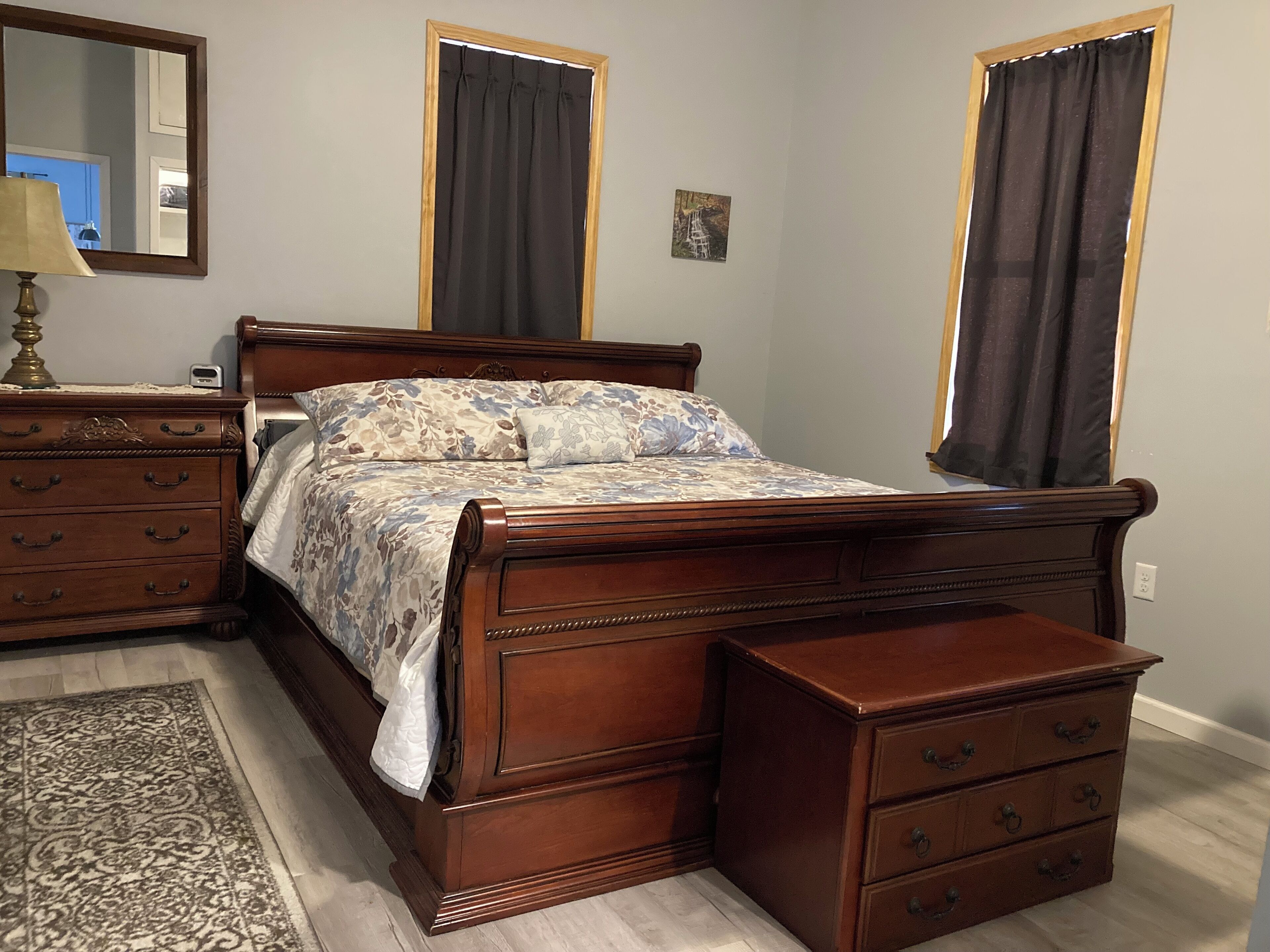 A bedroom with a wooden bed, a nightstand, a dresser, and a mirror.