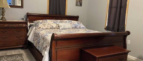 A bedroom with a wooden bed, a nightstand, a dresser, and a mirror.