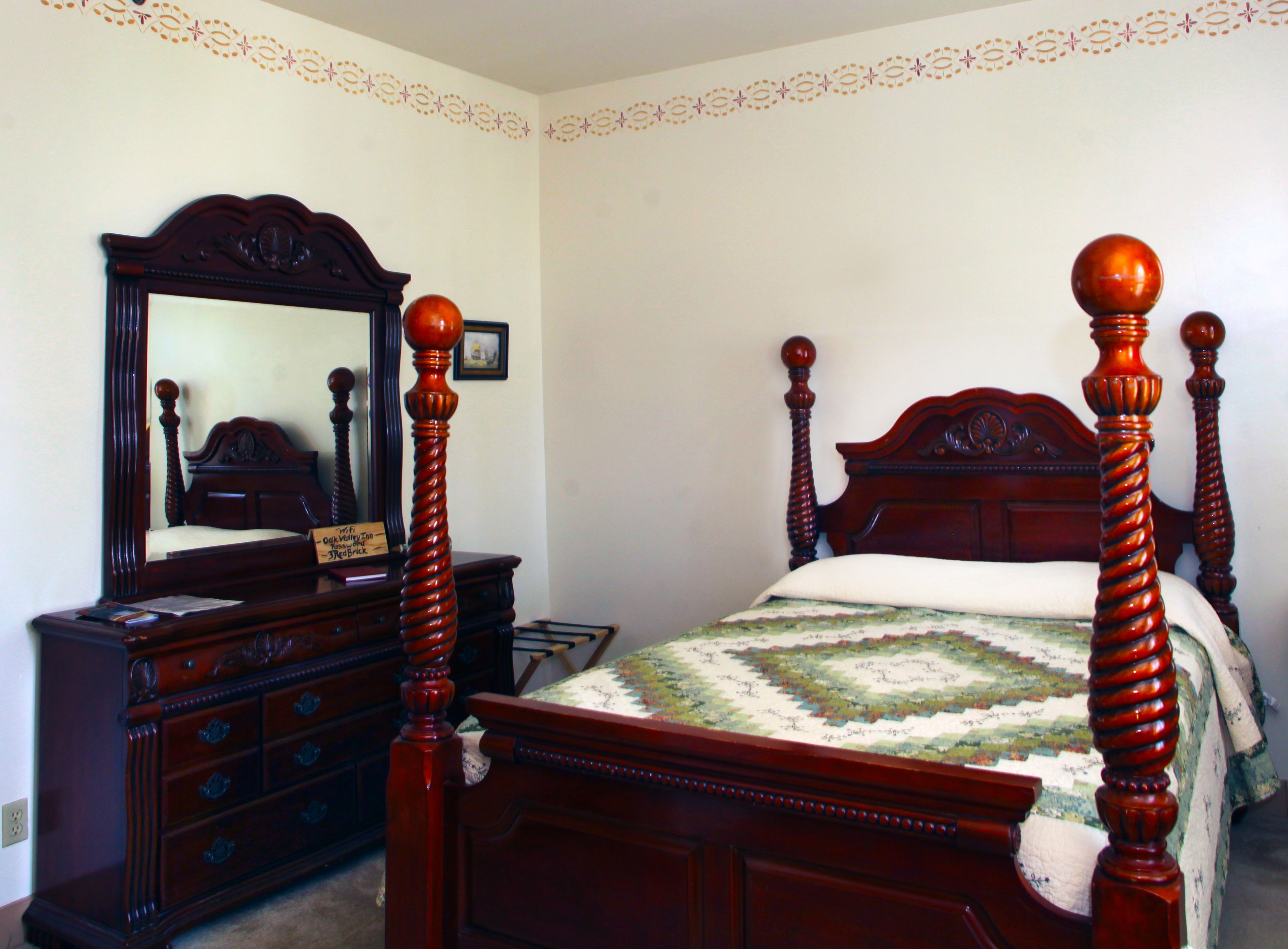 A bedroom with a wooden four-poster bed, a dresser, and a mirror.