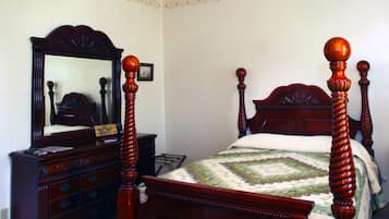 A bedroom with a wooden four-poster bed, a dresser, and a mirror.