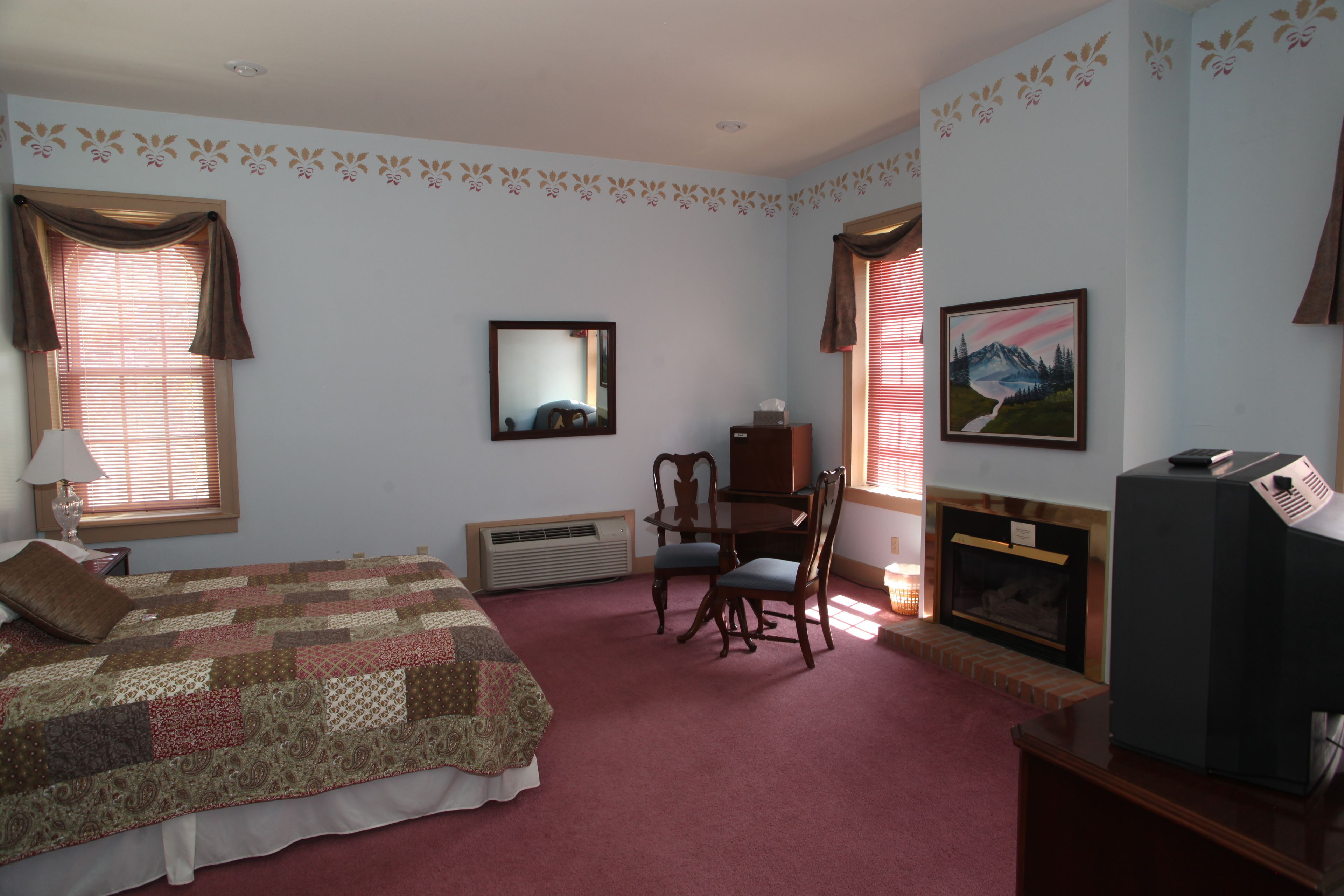 A bedroom with a bed, a desk, a chair, a fireplace, and a television.