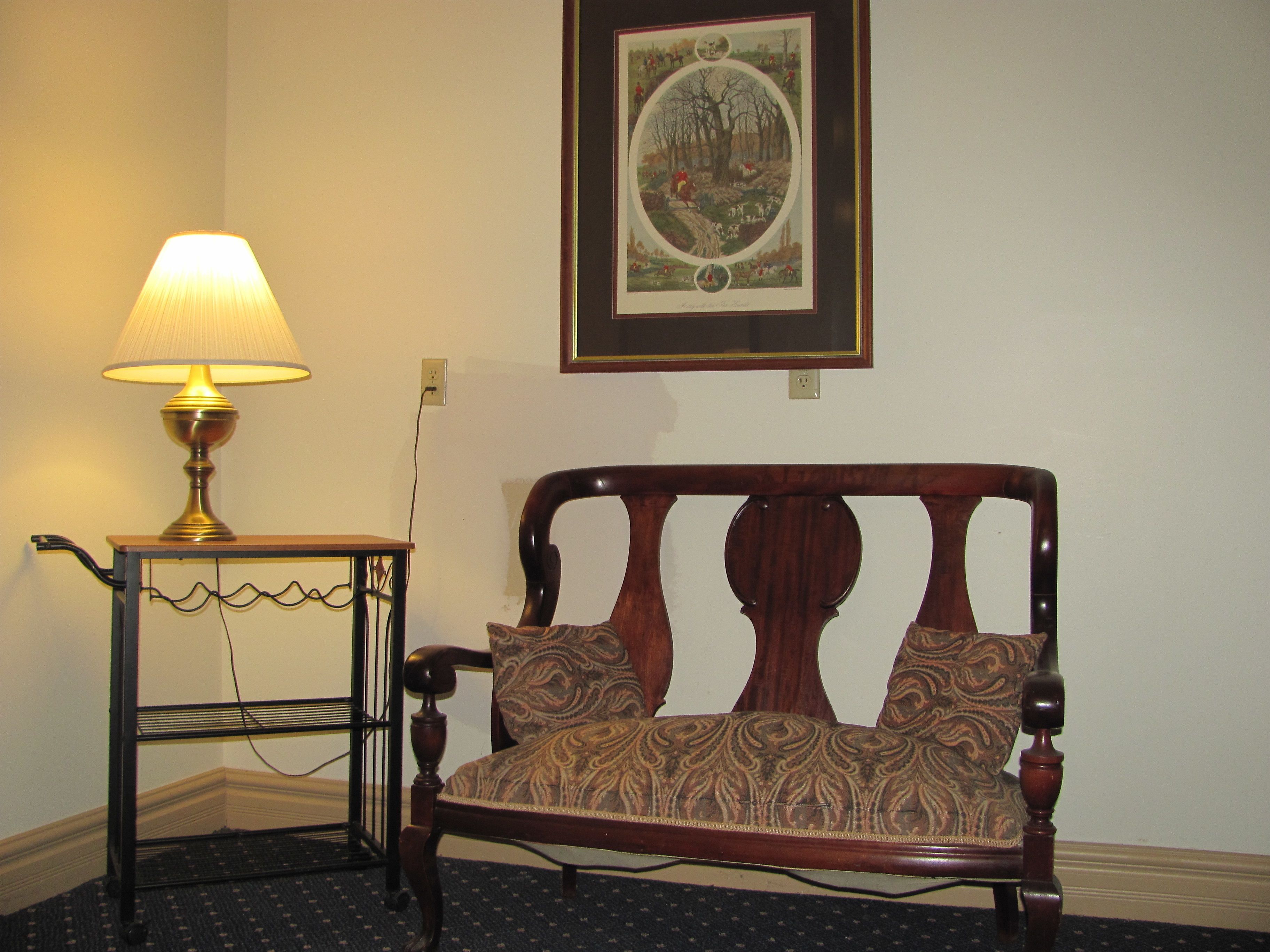 A room with a wooden bench, a lamp, and a framed picture on the wall.