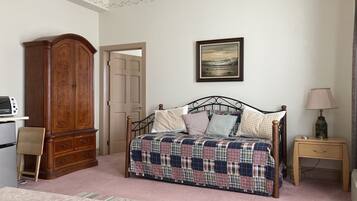 A bedroom with a bed, a wooden wardrobe, a desk with a computer, and a bedside table with a lamp.