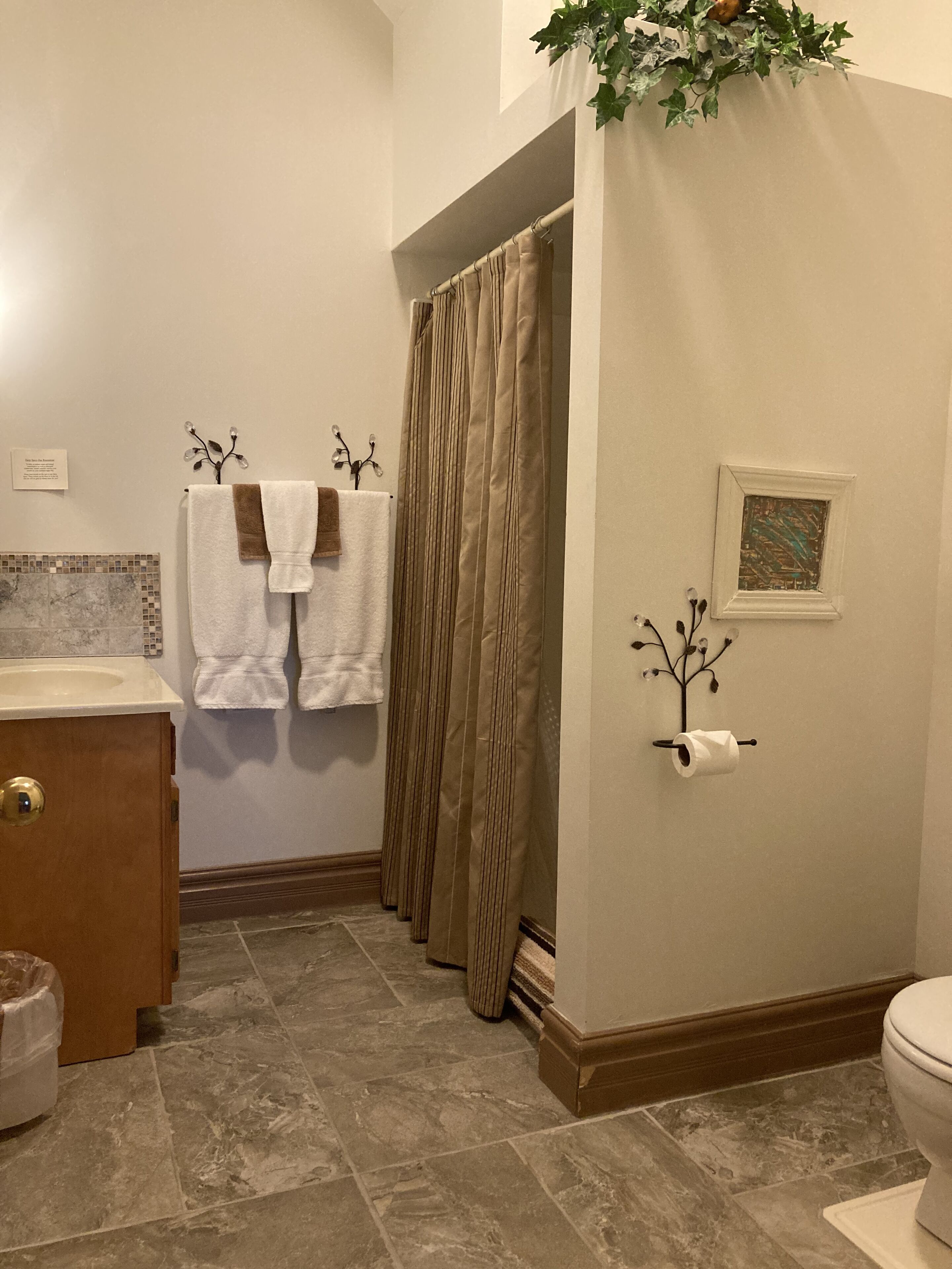 A bathroom with a toilet, sink, and shower curtain. There are towels hanging on the wall and a framed picture.