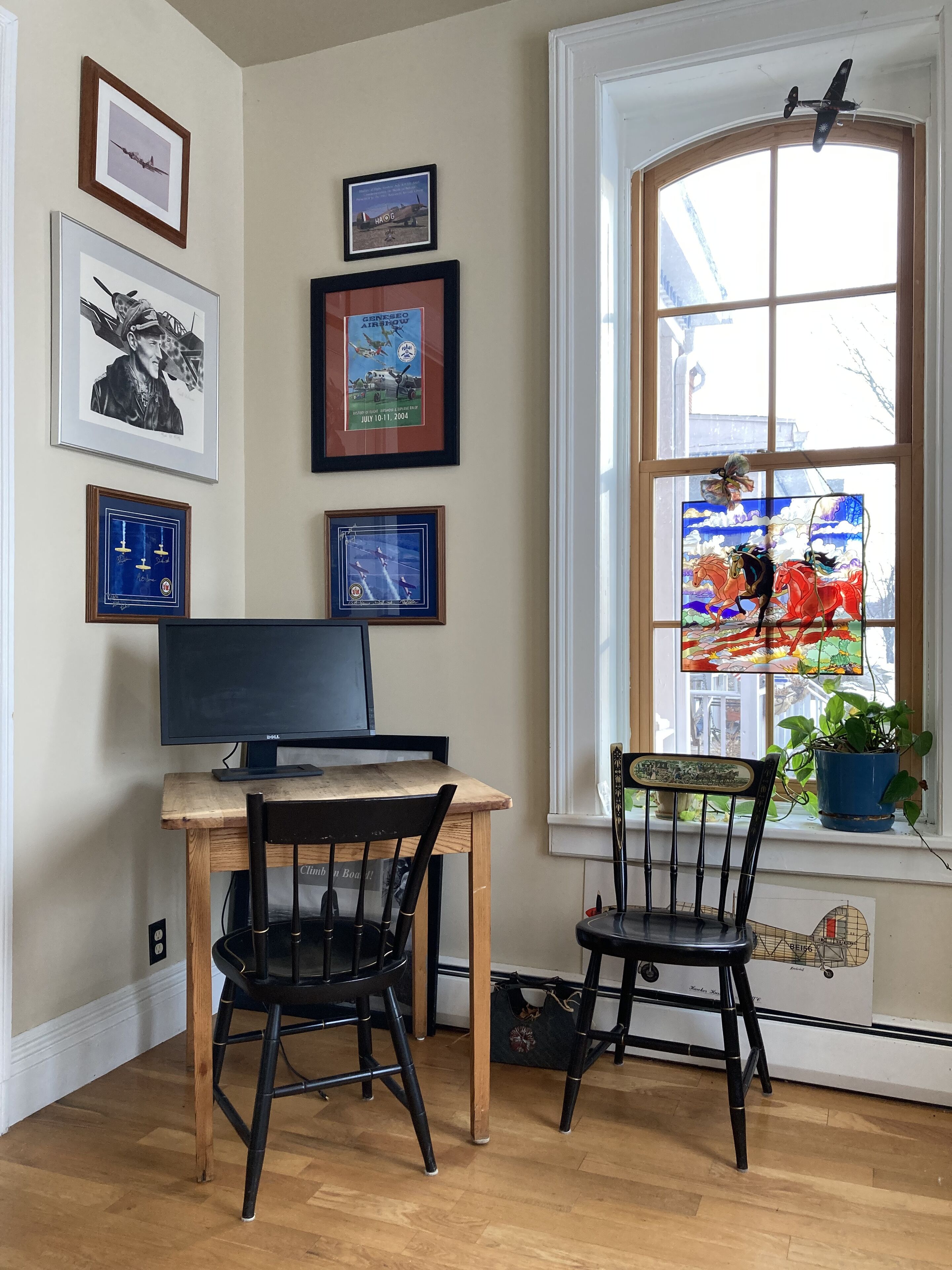 A room with a wooden desk, two black chairs, a computer, and a window with a view of a colorful street scene.