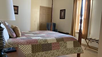 Un dormitorio con una cama con dosel, una silla, un escritorio con lámpara y una ventana con cortinas.