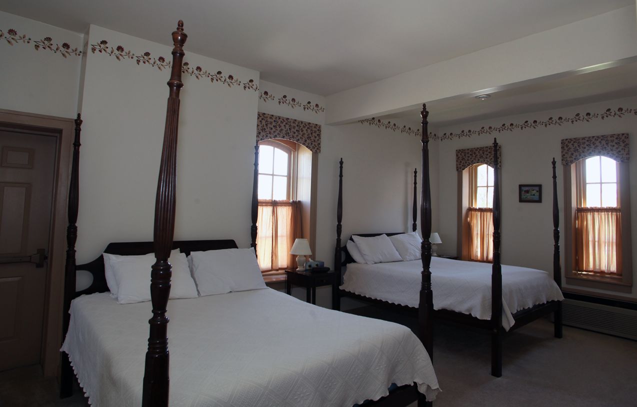 A traditional bedroom with two four-poster beds, a door, and windows with curtains.