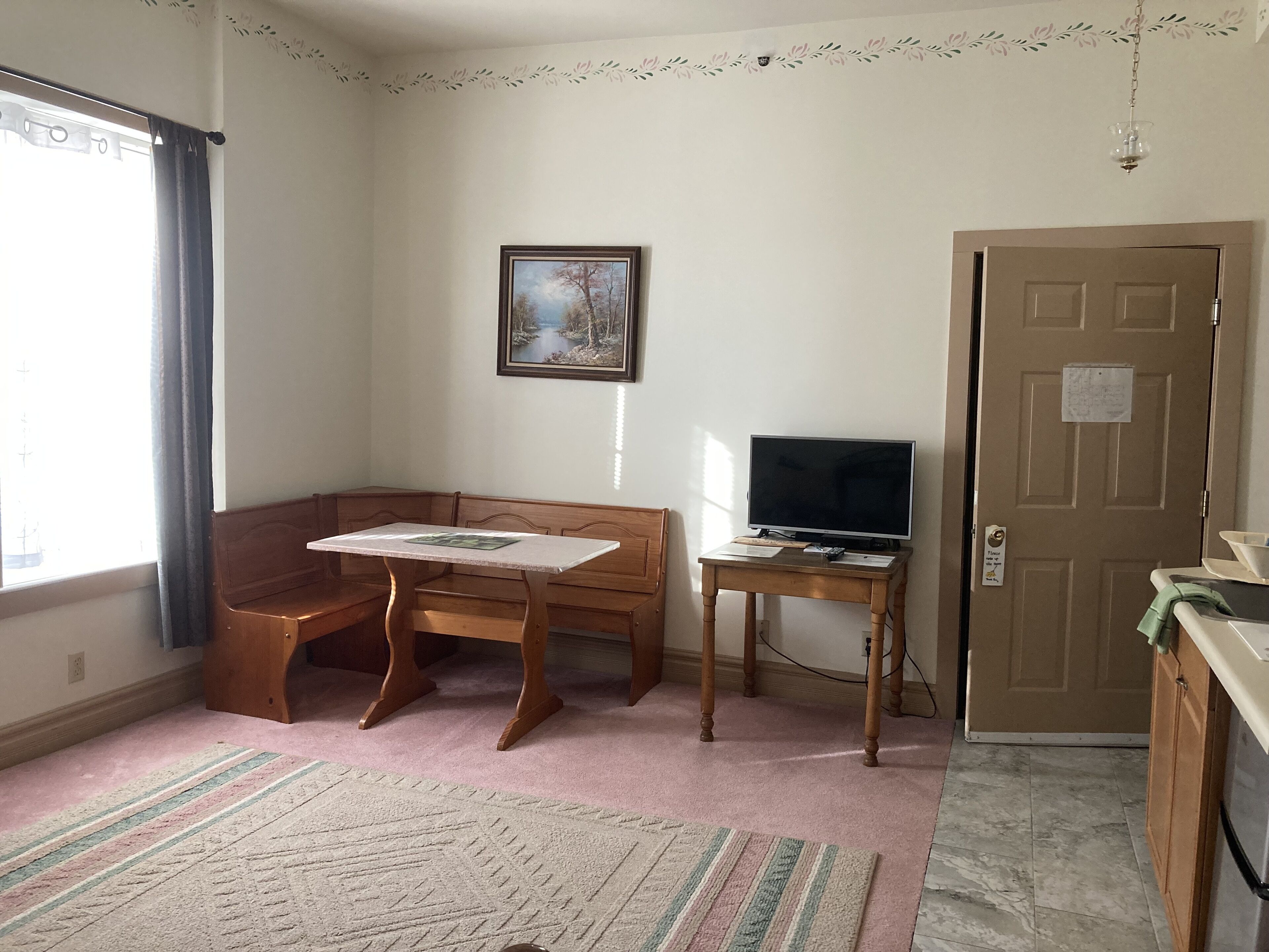 A room with a wooden bench, a small table, a television on a stand, and a door with a sign.