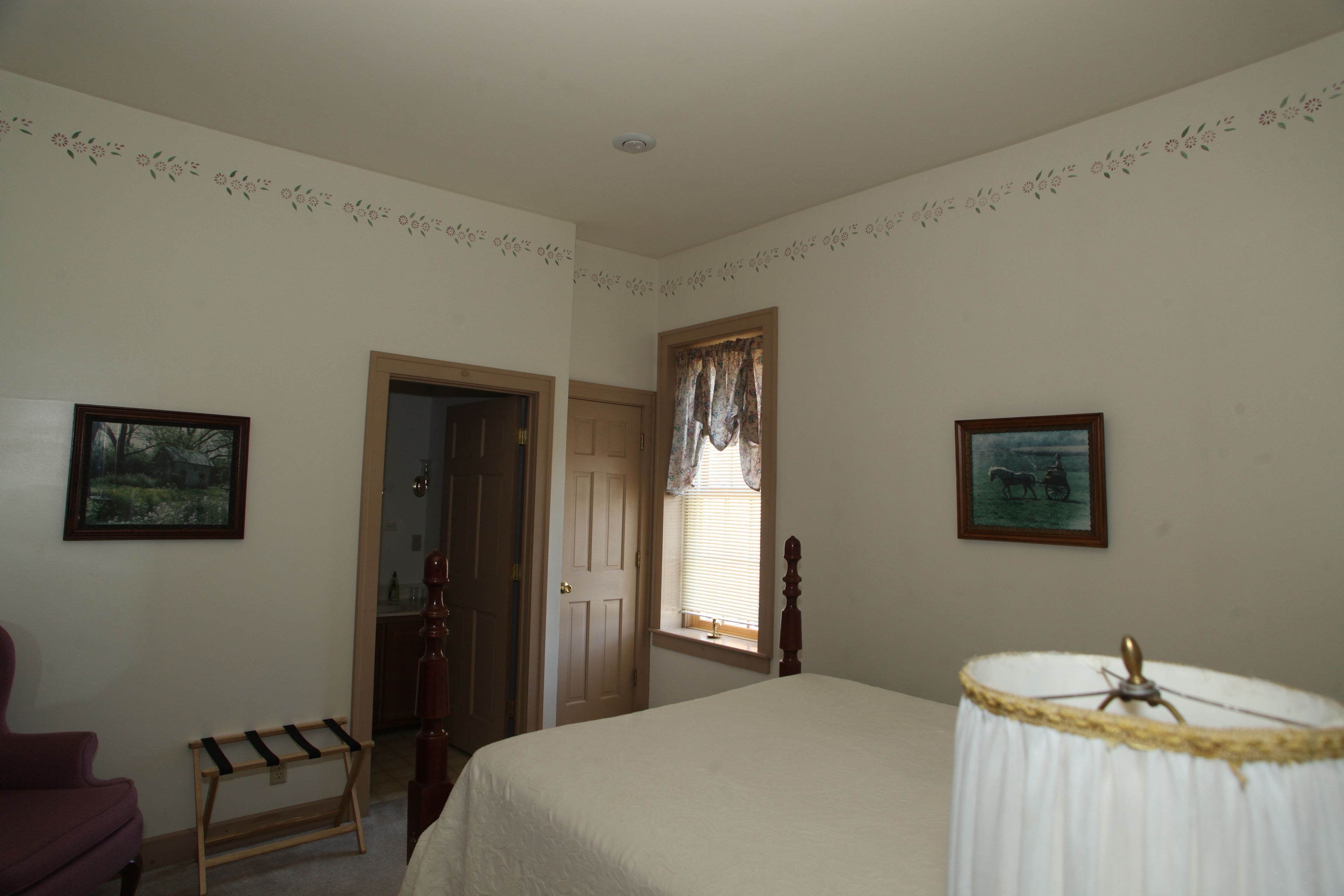 A bedroom with a bed, a chair, a door, and two framed pictures on the wall.
