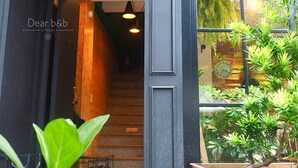 Una entrada de edificio moderno con una escalera de madera que conduce al interior, una puerta negra y un gran ventanal con vistas a zonas verdes.