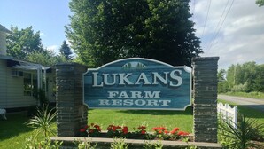Een bord voor Lukans Farm Resort met een stenen boog en een tuin met rode bloemen.