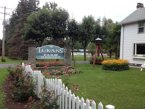Ein Schild für Lukans Farm Resort, umgeben von einem weißen Zaun, Blumen und einem Vogelhaus.