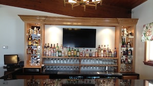 Een bar met een houten toog, diverse drankflessen en een televisiescherm.