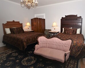 A hotel room with two beds, a chaise lounge, a small table with a lamp, and a chandelier.