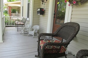 A porch with wicker chairs, a mailbox, and a white rocking chair.