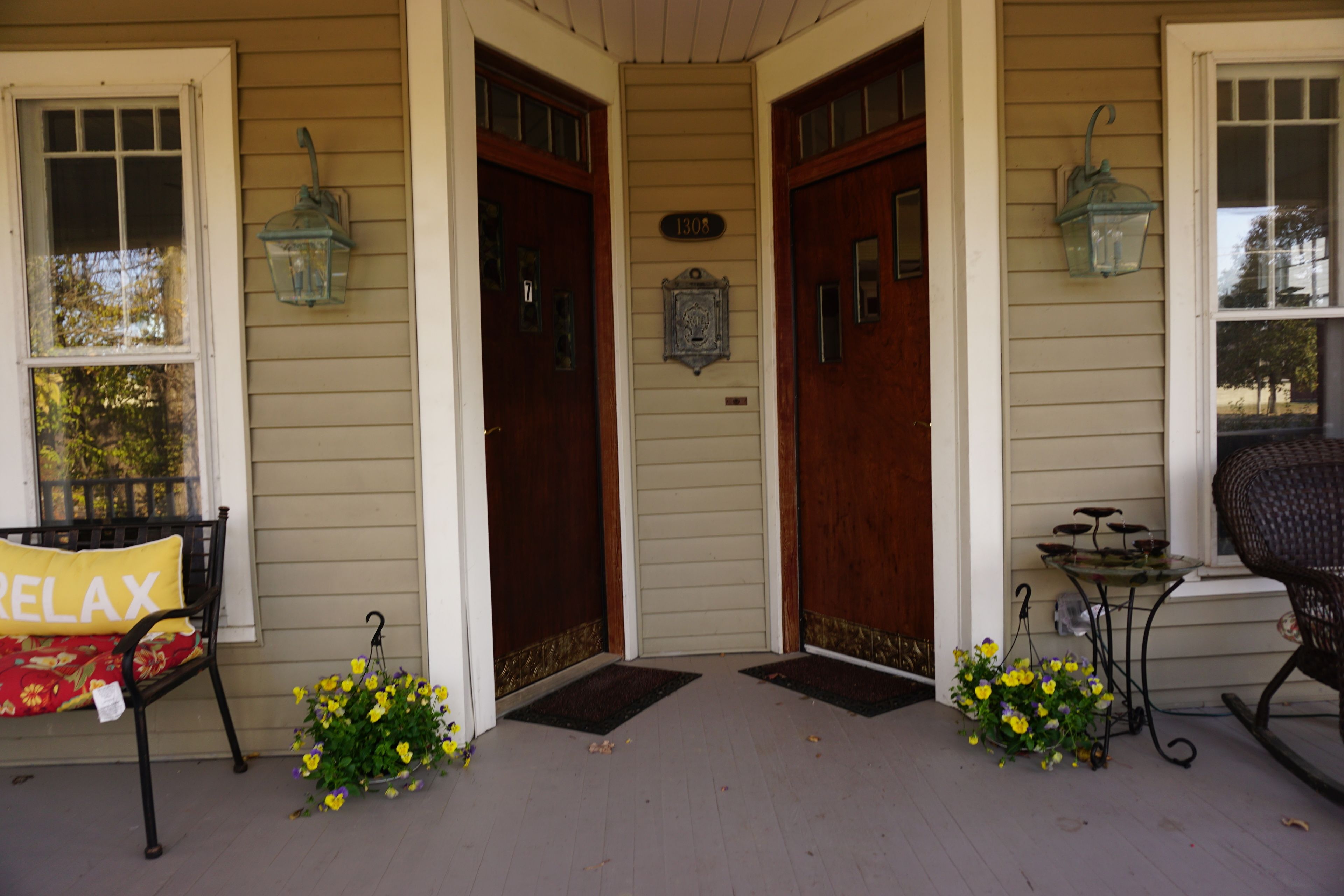 A porch with a bench, two doors, and a small table with flowers.