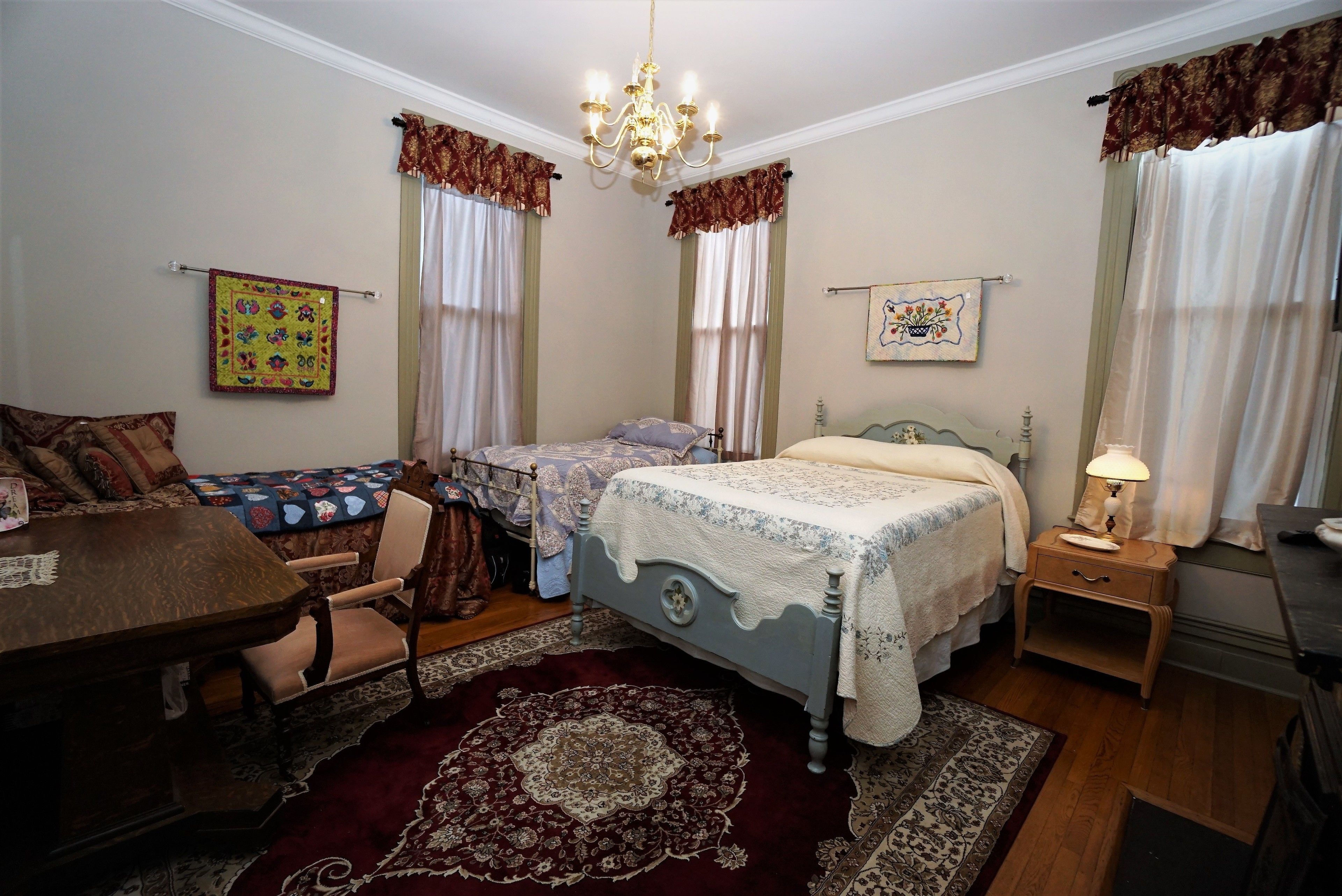 A bedroom with a bed, a desk, a chair, a nightstand, and a chandelier.