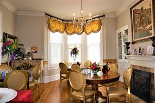 A dining room with a chandelier, gold chairs, a wooden table, and a fireplace.