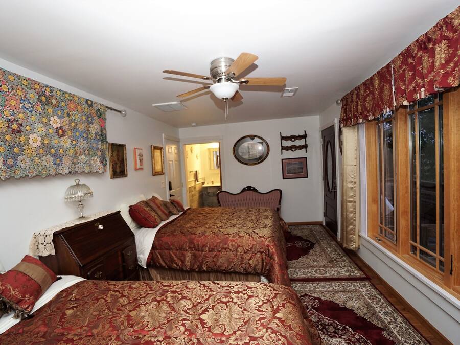 Un dormitorio con dos camas, un ventilador de techo, un tapiz floral grande y una ventana con cortinas.