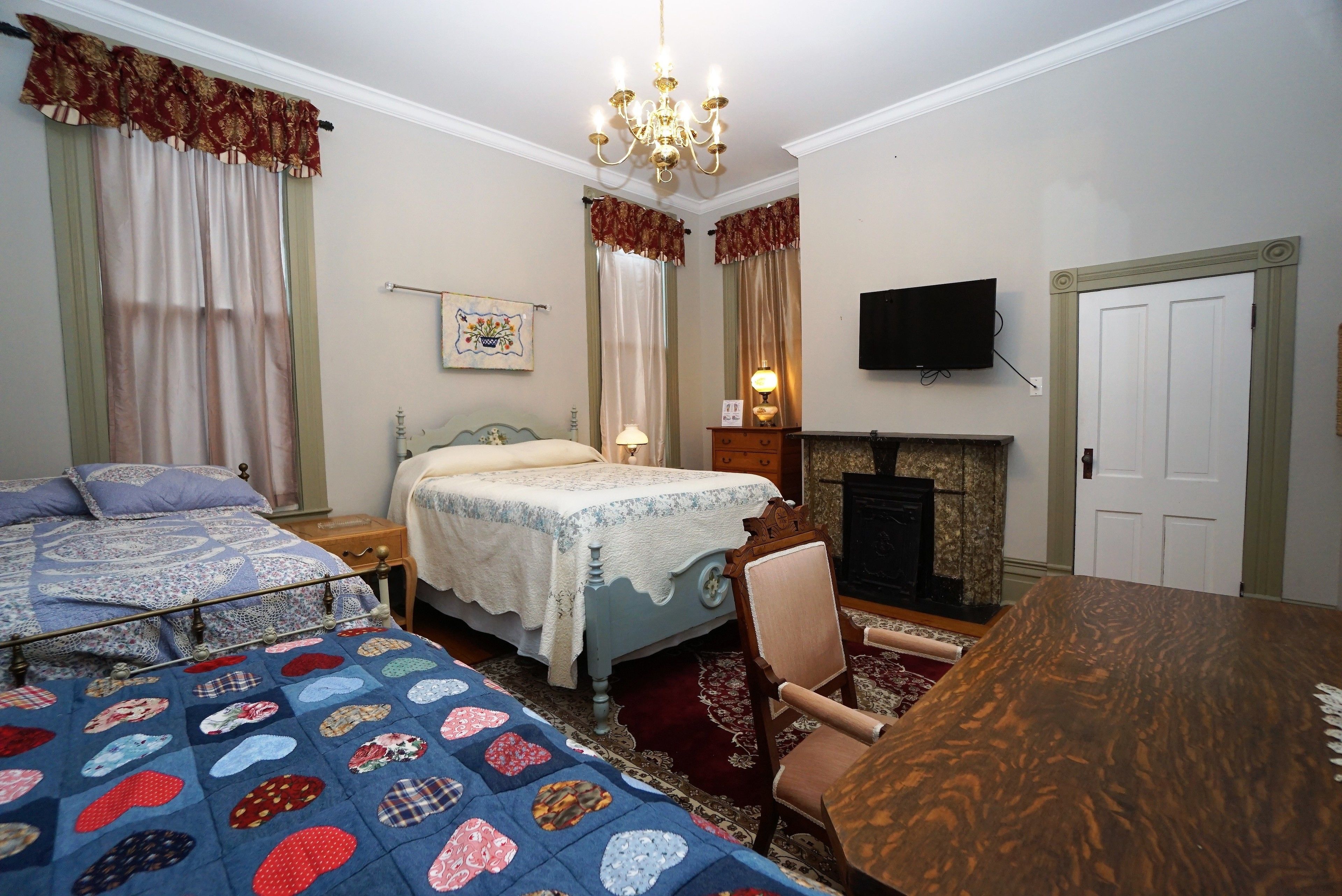 Un dormitorio con dos camas, una mesa de madera, una silla, una chimenea y un televisor en la pared.