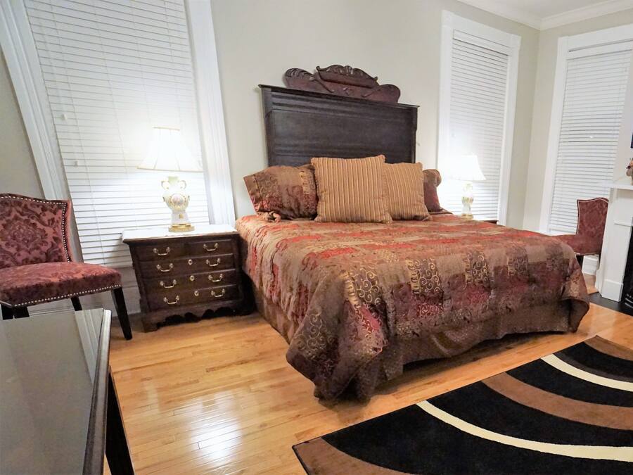 A bedroom with a large bed, a dresser, a chair, a television, and a fireplace.